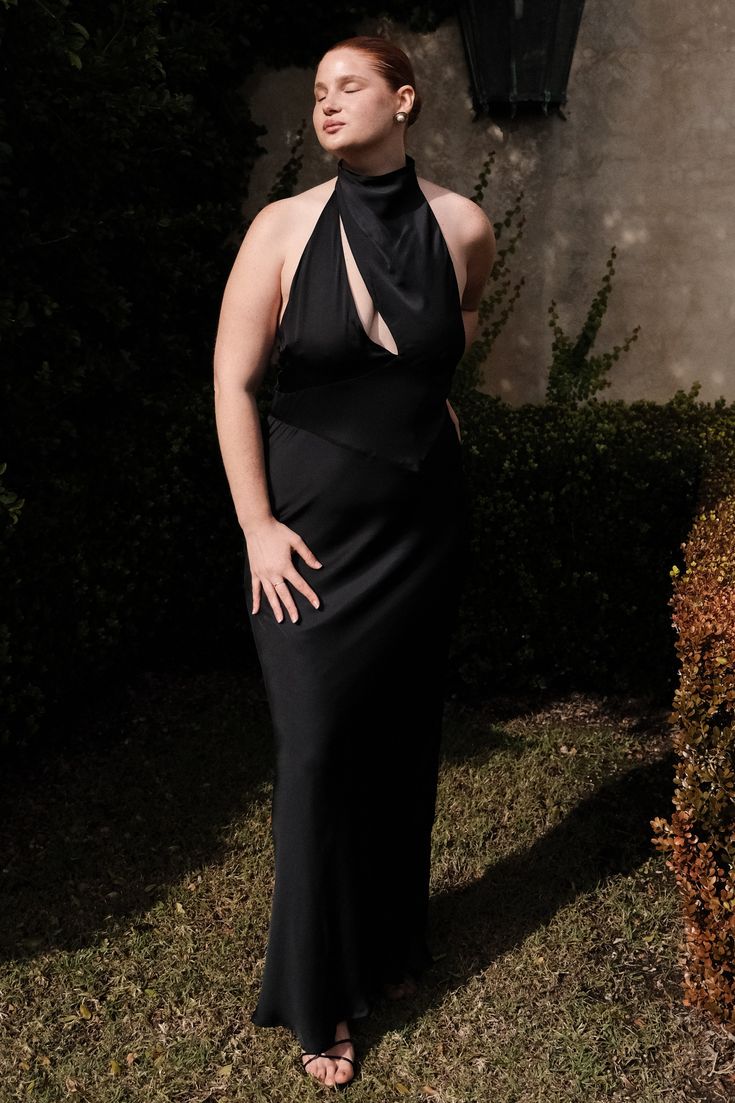 a woman wearing a black dress standing in the grass