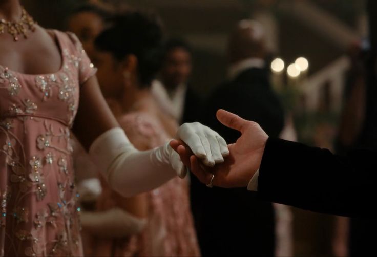 a man in a tuxedo and gloves is handing something to a woman wearing a pink dress