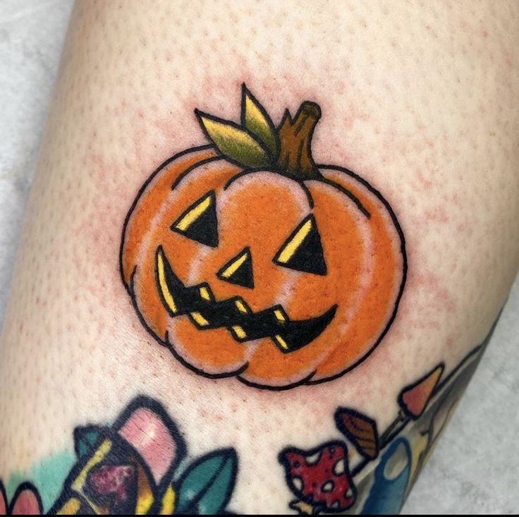 a close up of a person's leg with a pumpkin tattoo on the thigh