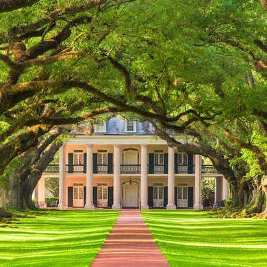 a large white house surrounded by trees on a lush green lawn with red brick walkway