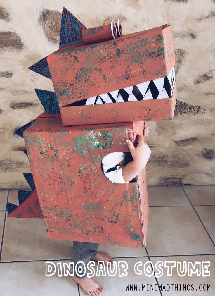 a young child is standing in front of a cardboard dinosaur costume