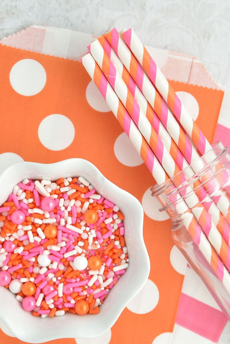 a bowl filled with sprinkles next to two pink and white drinking straws