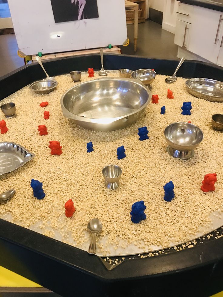 an assortment of metal bowls and spoons on top of sand in a play area