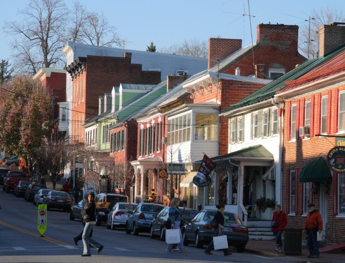 people are walking down the street in front of some buildings and cars parked on the side of the road