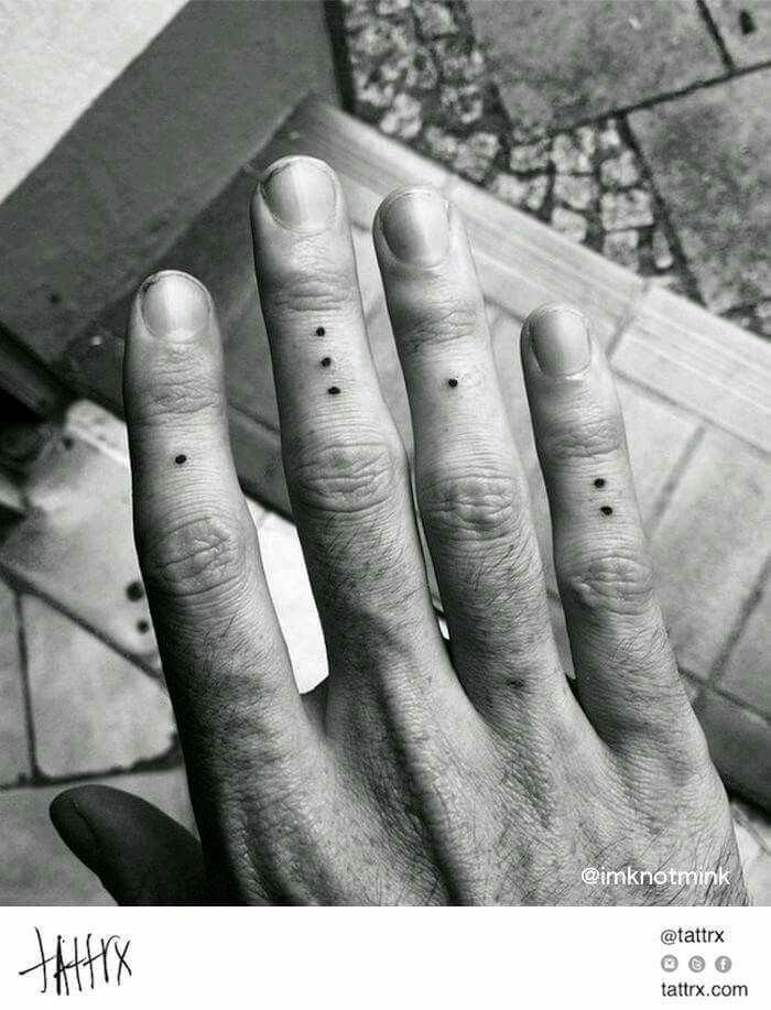 a person's left hand with two small dots on the middle finger and an arrow tattoo