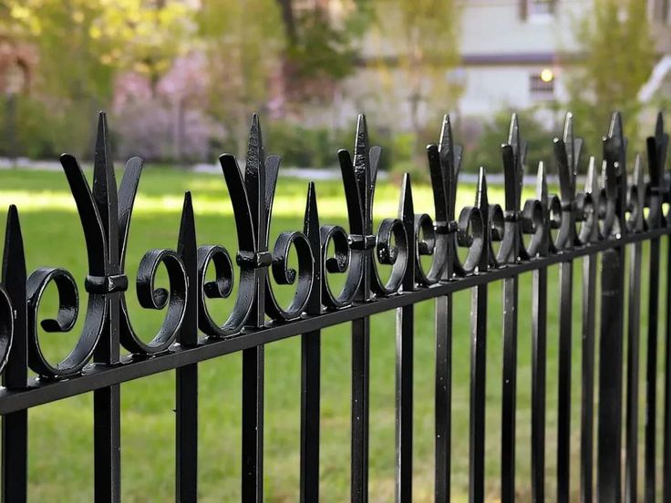 an iron fence in front of a green lawn