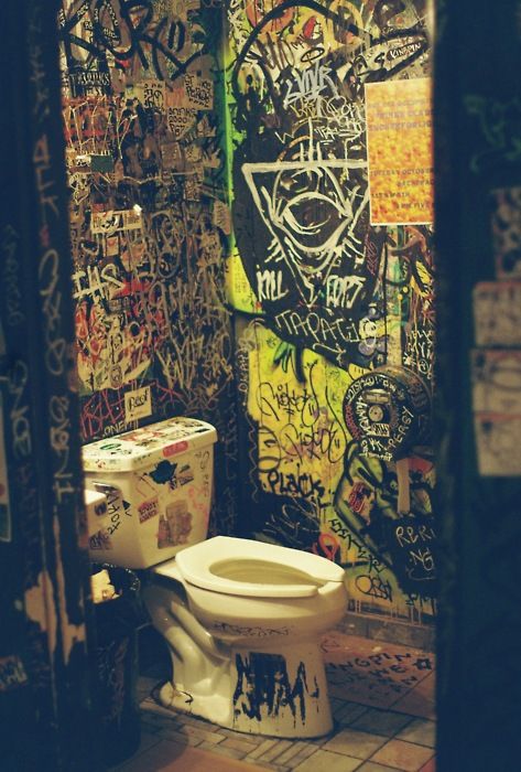 a bathroom with graffiti all over the walls and toilet seat lid up in front of it