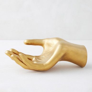 a gold colored hand holding something in it's right hand on a white surface