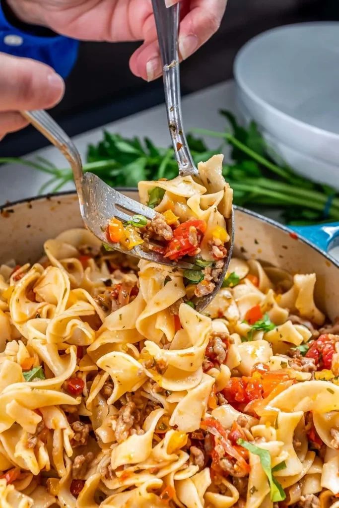 someone is holding a fork full of pasta with meat and vegetables on it in a skillet