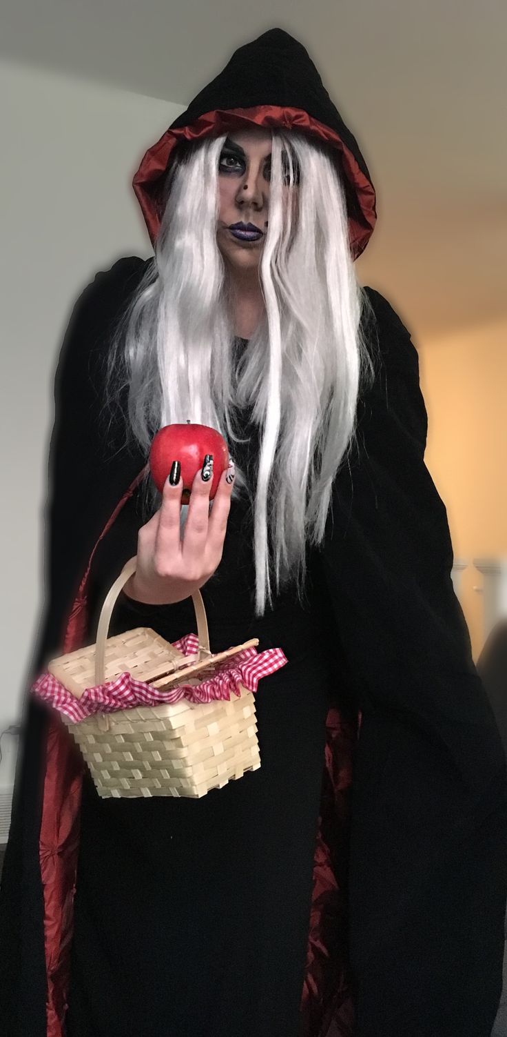 a man dressed as a witch holding a basket with an apple in it and wearing makeup