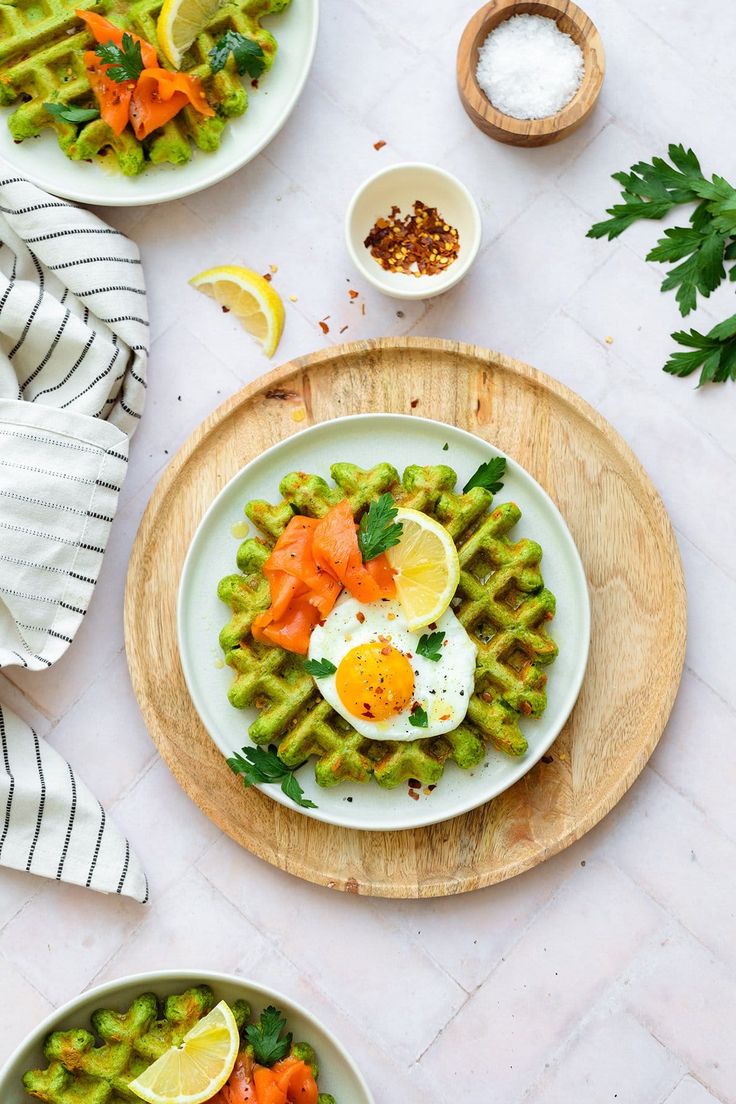 two plates with waffles topped with eggs and vegetables