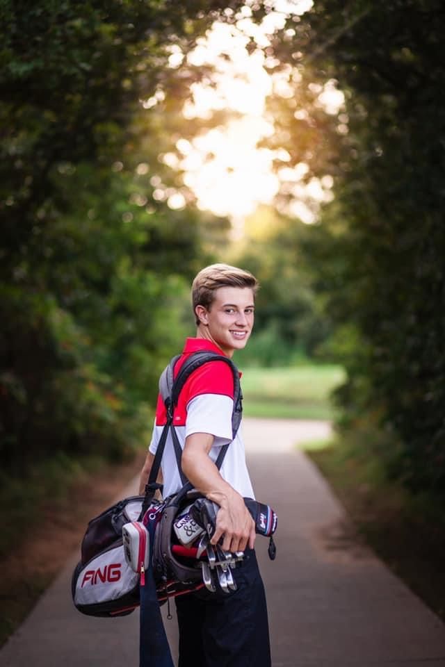 a young man is holding his golf gear and smiling at the camera while standing on a path