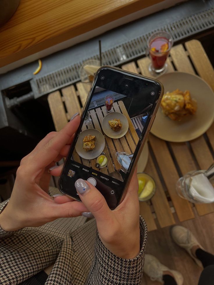 a person holding up a cell phone with food on the table in front of them