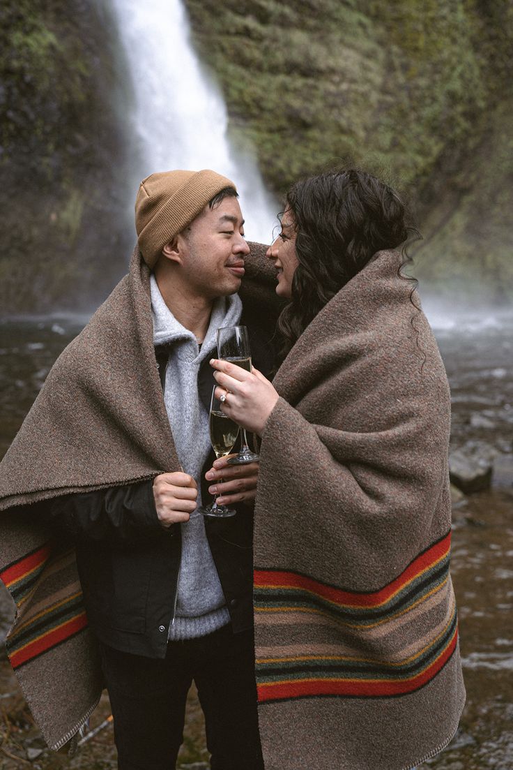 two people standing next to each other under a waterfall with a blanket over their heads