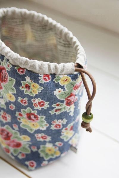 a small blue flowered fabric basket on a white table with a brown string around it