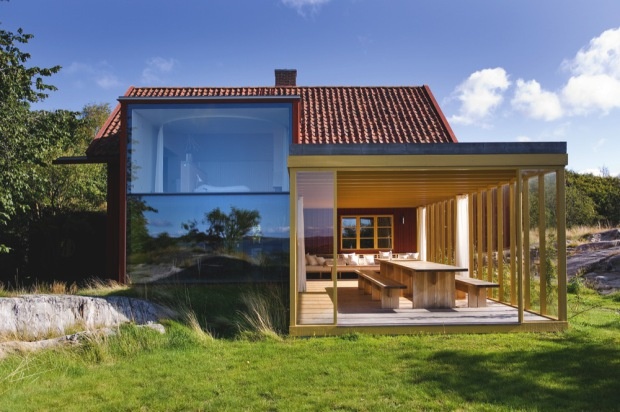 the house is surrounded by green grass and has a large glass door that leads to an outdoor dining area