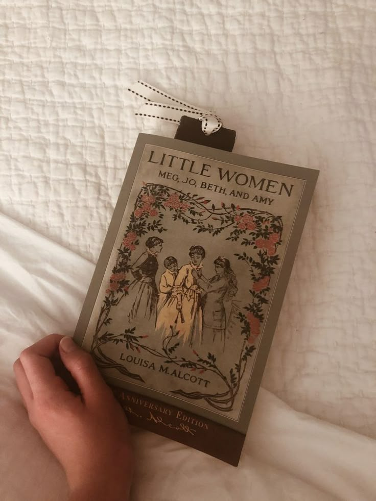 a hand holding a book on top of a bed