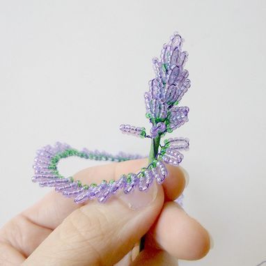 a hand holding a tiny purple flower in it's left side, with beads on the end