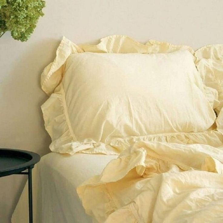 a white bed topped with pillows next to a small table and vase filled with flowers