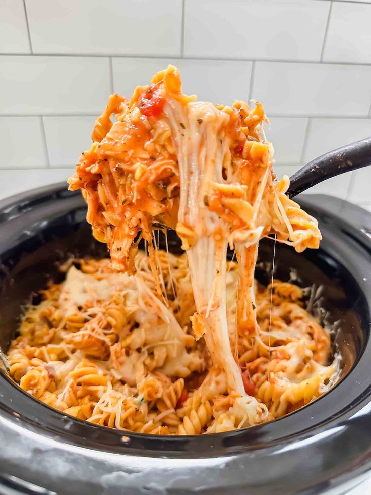 the pasta is being lifted from the slow cooker with a spatula in it