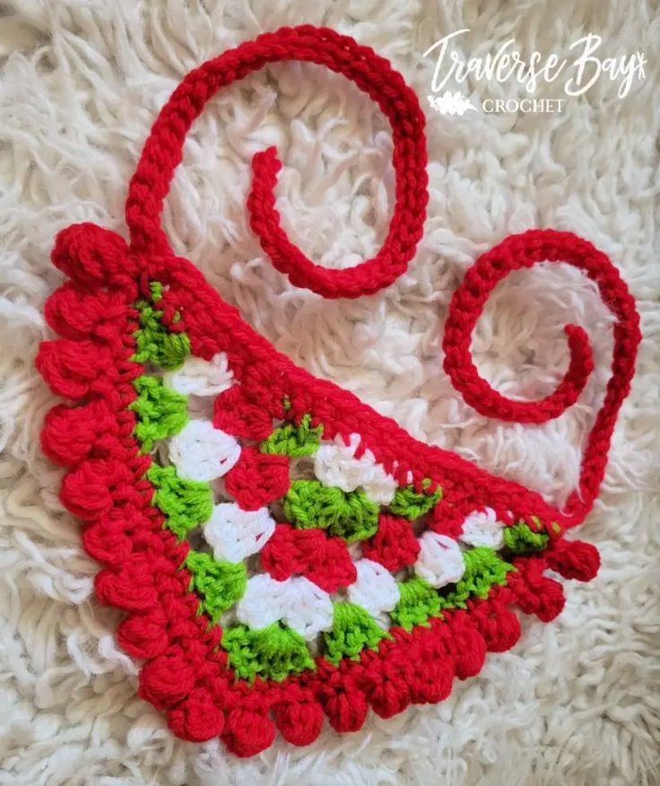 a crocheted christmas ornament is laying on a white blanket with red and green trim