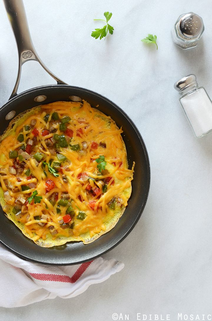 an omelet with cheese and vegetables in a skillet on a white table