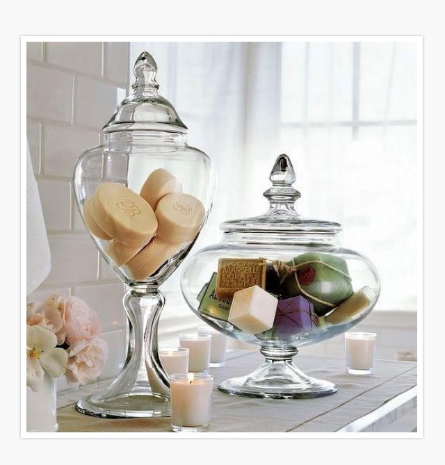 two glass jars filled with soaps and candles on a table next to some flowers