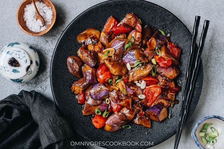 a black plate topped with meat and veggies next to chopsticks on a table