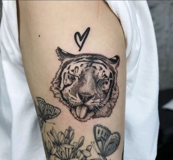 a black and white tiger tattoo on the left upper arm with flowers in the background