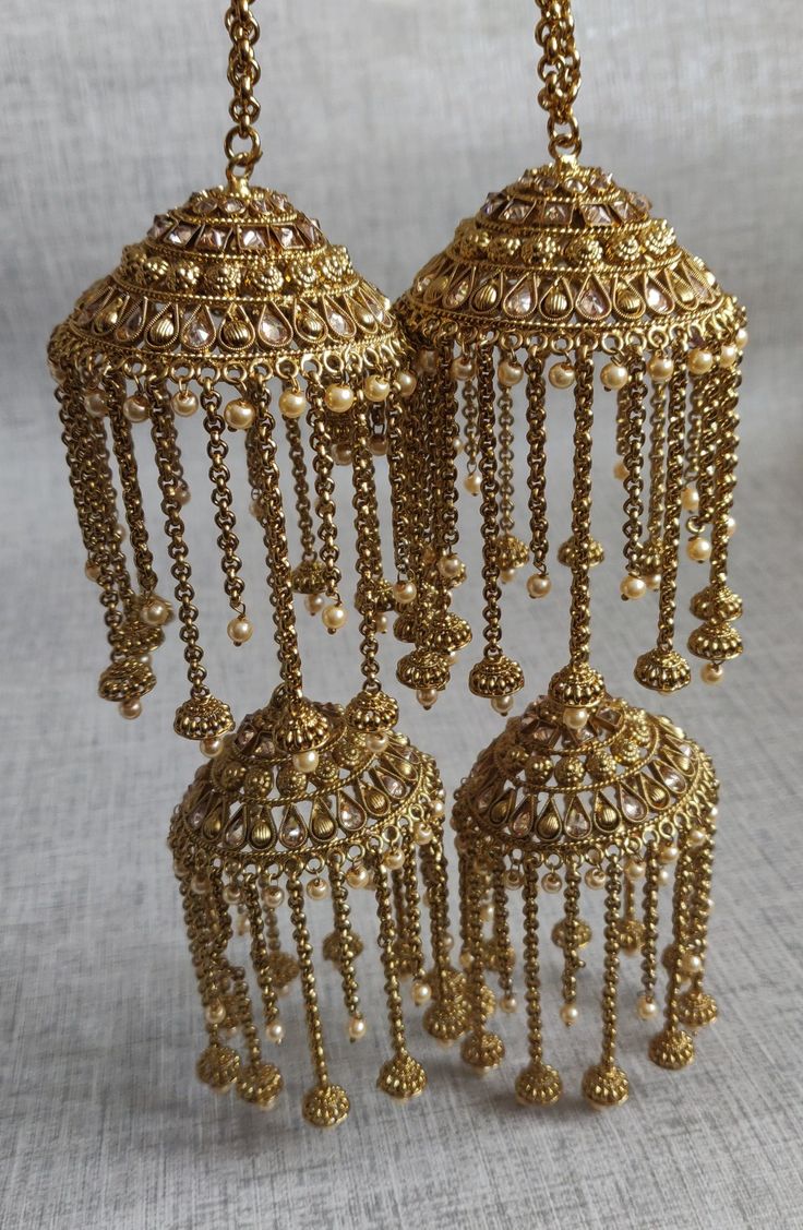 three golden chandeliers hanging from chains on a white cloth covered table with a gray background