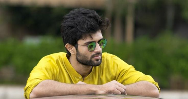 a man in yellow shirt and green sunglasses leaning on top of a car with his arms crossed