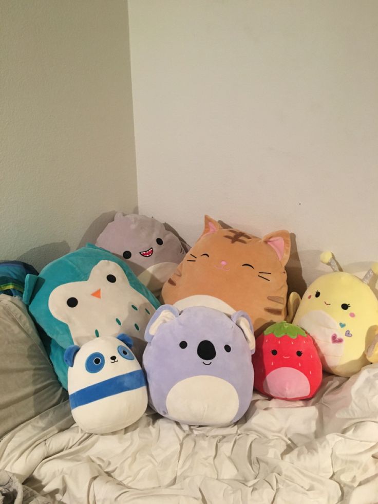 a bunch of stuffed animals sitting on top of a white sheet covered bed next to a wall