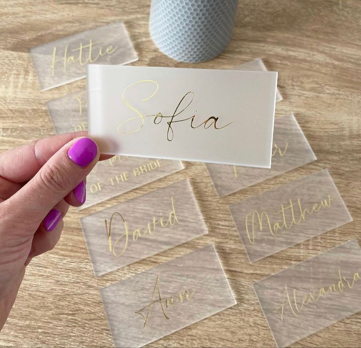 a person holding up a business card on top of a wooden table next to a cup