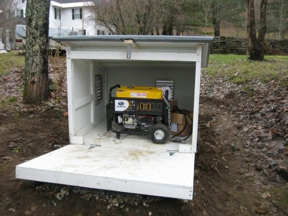 a small portable generator sits in the back of a white shed with trees around it