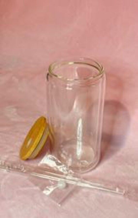 an empty glass jar with a yellow lid on a pink table cloth next to a measuring spoon