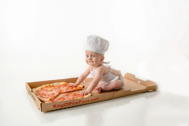 a baby in a chef's hat sitting on top of a box with pizza