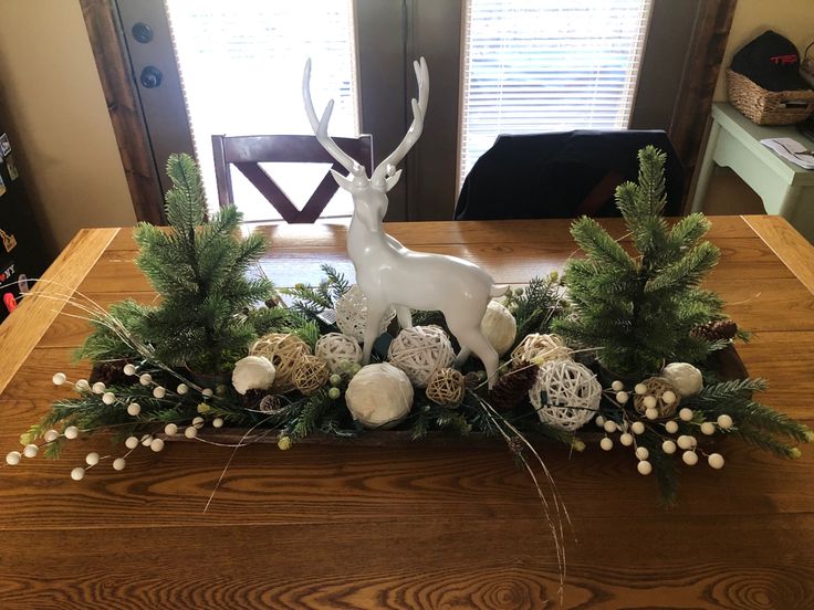 a wooden table topped with white balls and greenery next to a deer figurine