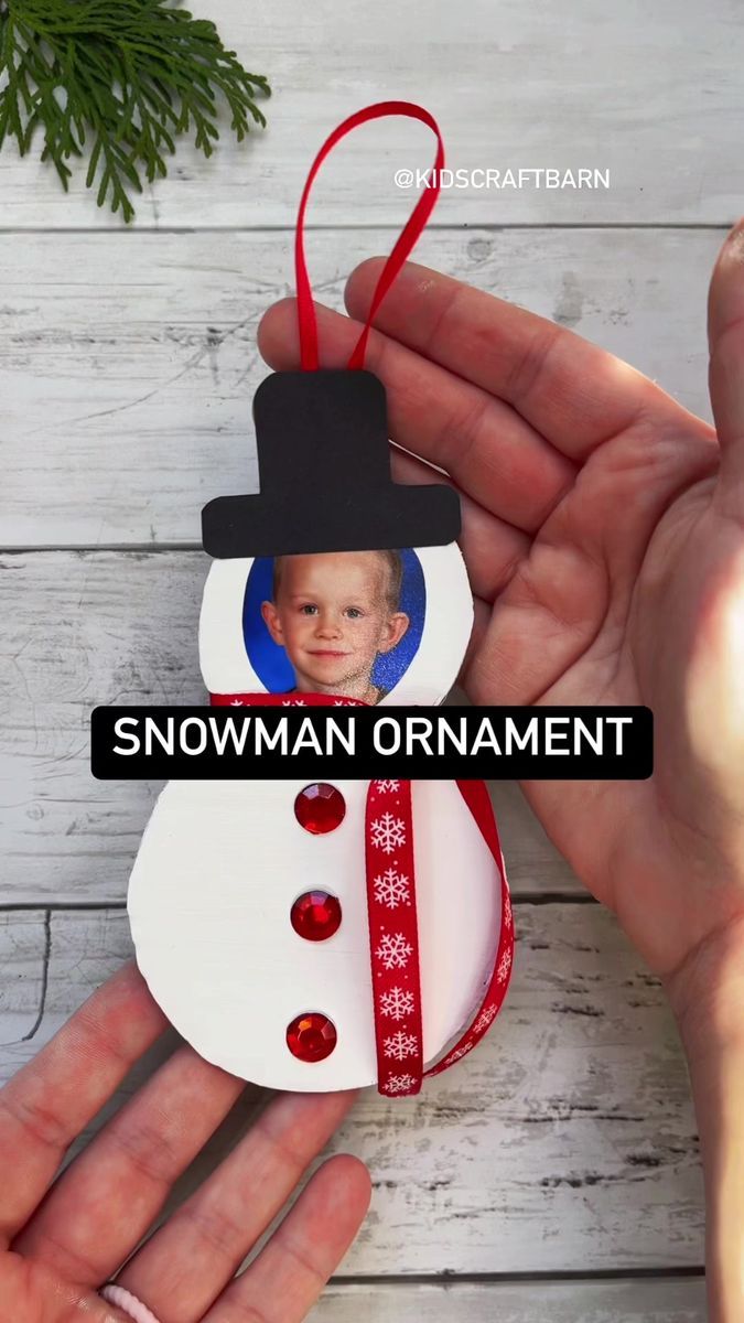 a hand holding a small snowman ornament with a red ribbon around it