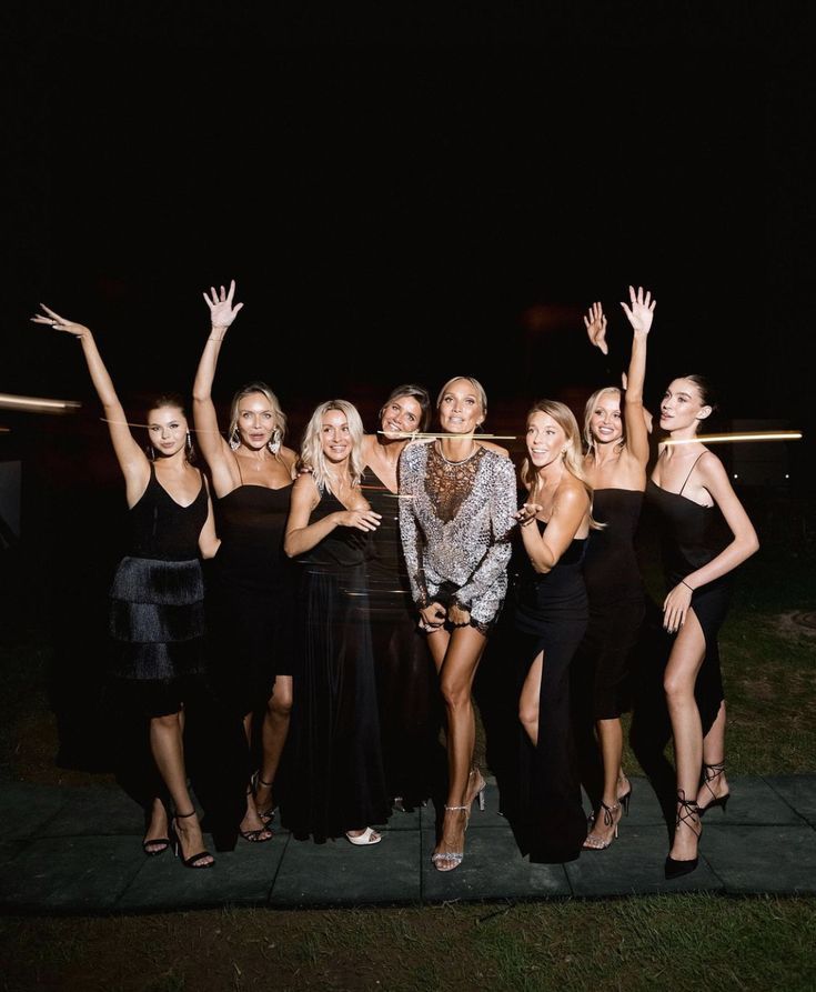 a group of women standing next to each other in front of a black background at night