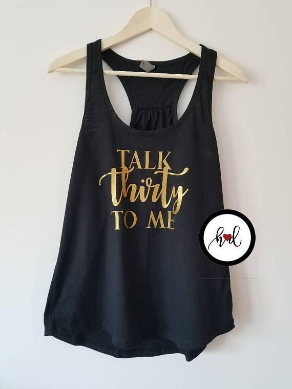 a black tank top with gold lettering that says talk thirty to me on it, hanging from a hanger