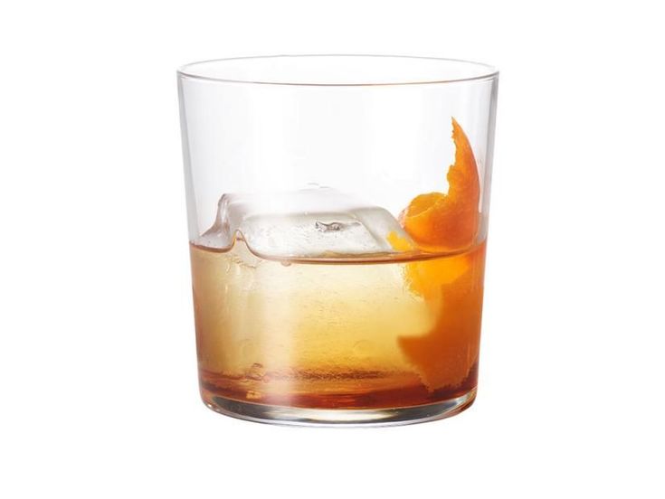 an old fashioned glass filled with ice and orange peels on the rim, sitting on a white surface