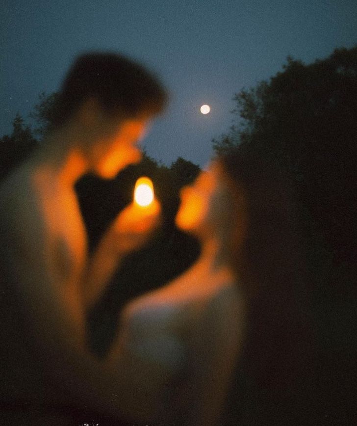 two people standing next to each other in front of a full moon at night with one holding a cell phone