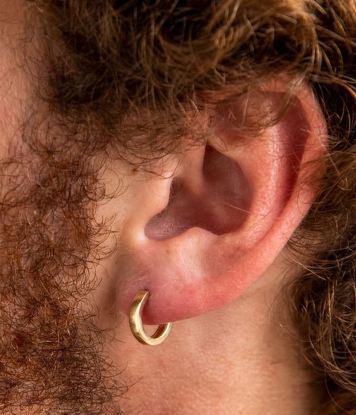 a man with curly hair wearing a pair of gold hoop earrings on his left ear