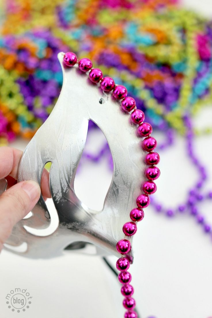 someone is holding a silver mask with pink beads on it and there are other colorful beads in the background