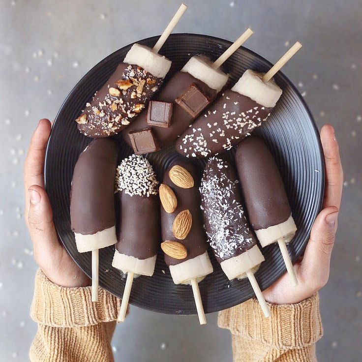 a person holding a black plate with chocolates and almonds on it in their hands