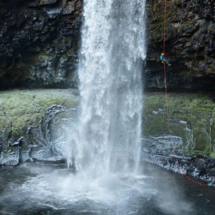 a man climbing up the side of a waterfall with a rope attached to his waist