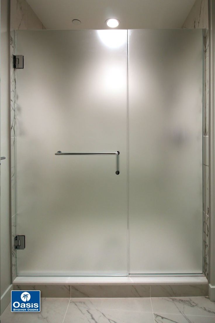 a bathroom with a glass shower door and white tile flooring, along with a light on the wall