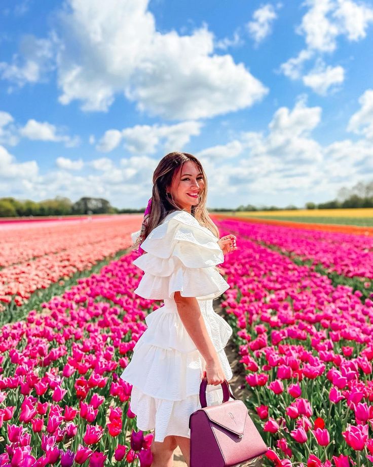 a woman standing in a field full of pink tulips holding a purple purse