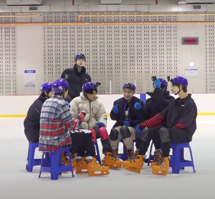 several people sitting on stools in an ice rink with helmets and gloves around their necks