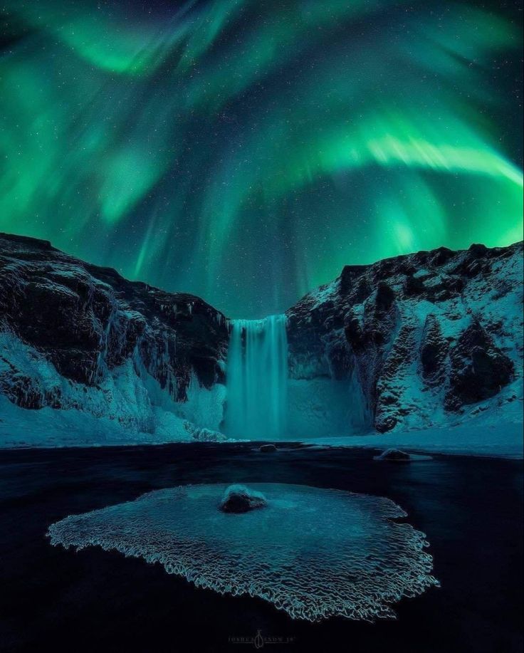 the aurora bore is lit up in the night sky above a waterfall and snow covered mountains